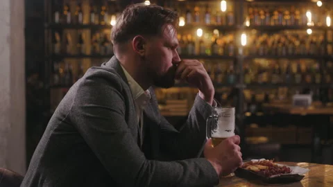 A man is sitting in a pub, drinking beer. He looks disappointed and is Video stock 238911395