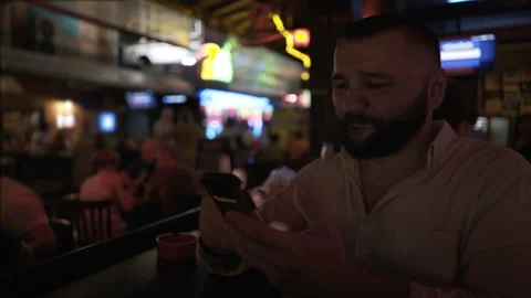 Man sitting in pub at the evening and browsing internet on smartphone Stock Footage 90563819
