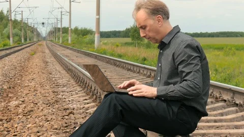 A man is sitting on the rails and working on a laptop. Stock Footage 77332718