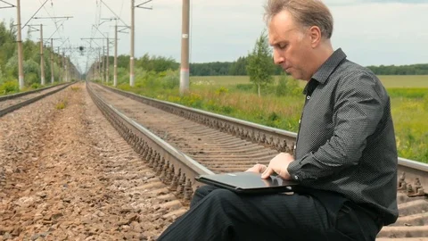 A man is sitting on the rails and working on a laptop. Stock Footage 77518812