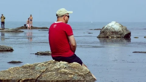A man is sitting on a reef looking at the sea Stock Footage 77457260