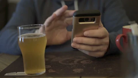 Man sitting in the restaurant and drinking beer while using smartphone Stock Footage 87543176