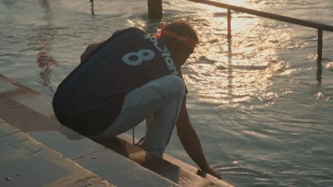 Man sitting on river steps touching water calm morning scene 스톡 동영상 332920786