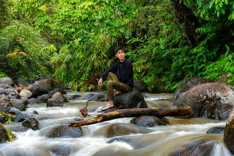 Man sitting on the river while looking around. Lonely man sitting on the rock Stock Photos