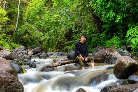 Man sitting on the river while looking around. Young man sitting alone in t.. Stock Photos