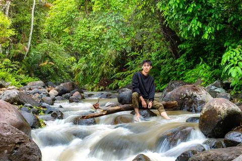 Man sitting on the river while looking at you. Handsome man sitting alone i.. Stock Photos