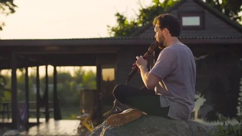 A man sitting on a rock and playing ethnic flute Video stock 84680127
