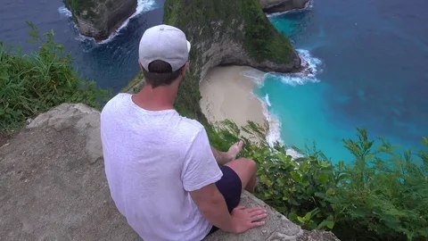 Man sitting on a rock at the edge of a cliff on Nusa Penida island in Indonesia Stock Footage 85375350