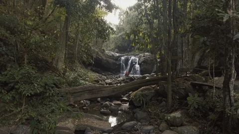 Man sitting on the rock in front of waterfall in tropical forest at early mor Stock Footage 86852892