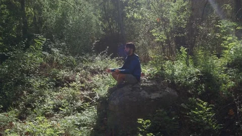 Man sitting on a rock in the middle of the forest sitting meditating. Stock Footage 139614023