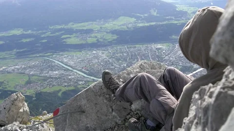 Man sitting on rocks on mountain looking down to urbanized valley Stock Footage 43811848