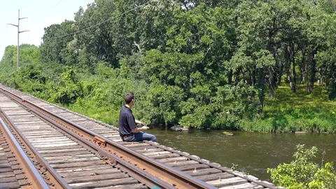 Man sitting on a rustic train bridge throwing rocks into a fast moving Stock Footage 93665942