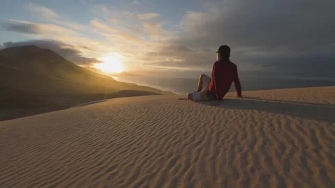Man Sitting on Sand Dune Watching Sunset Over Ocean Lanzarote 스톡 동영상 331268412
