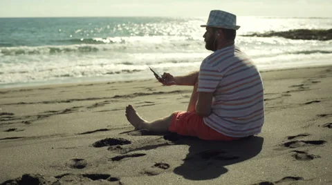 Man sitting on the sandy beach and listening music, steadycam shot Stock-Footage 60133572