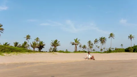 Man sitting on sandy beach in Goa India with palm trees and sky Stock Footage 348055593