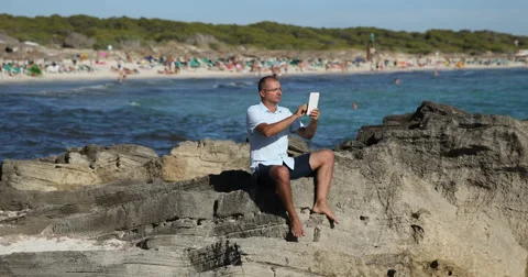 Man Sitting at Seaside and Reading News Online Digital Tablet Vacation Concept Stock Footage 67997218