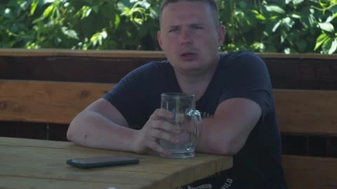 A man is sitting in the shade in a gazebo at a table. he drinks water from a mug Stock Footage 166777465