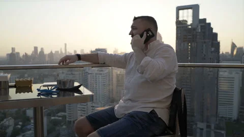 Man sitting in skybar during sunset and chatting on cellphone Stock Footage 90551757