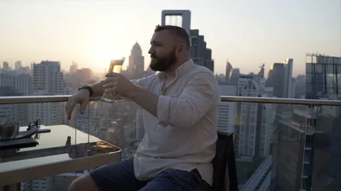 Man sitting in skybar during sunset and drinking beer  Stock Footage 90552462