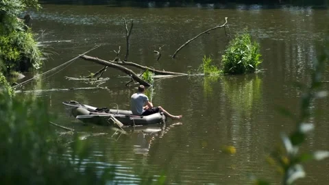 A man is sitting in a small boat on a river surrounded by trees and debris Stock Footage 329177228
