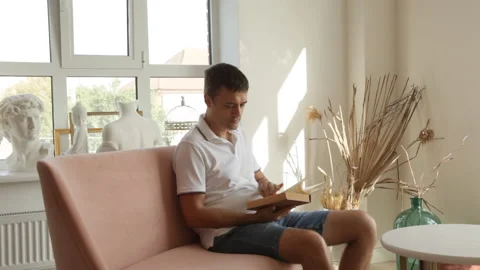 A man is sitting on a sofa and begins to read a book. Stock Footage 205611367