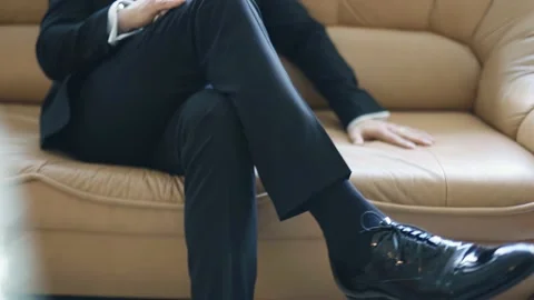 A man is sitting on the sofa and crossing his legs. Shooting in slow motion Stock Footage 201968817