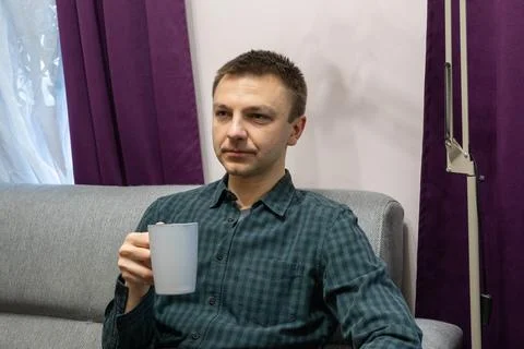 Man sitting on a sofa and holding a cup of hot drink. Relaxed guy resting 스톡 사진