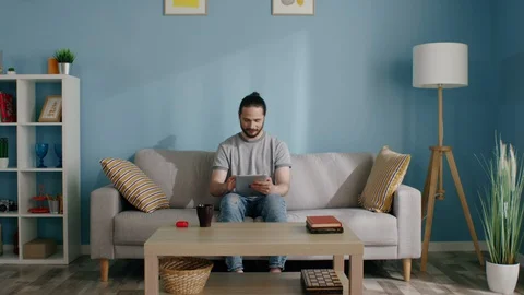Man Is Sitting on Sofa and Playing Game on Gadget Video stock 129895116