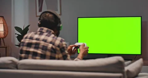 Man sitting at sofa and playing video games. Male holding joystick and wearing Stock Footage 272924337
