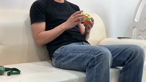 The man sitting on the sofa and practicing the cube Stock Footage 239887691