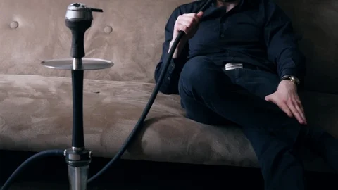 A man sitting on sofa and smoke hookah. Guy pulls out of his pocket red phone. Video stock 108003601