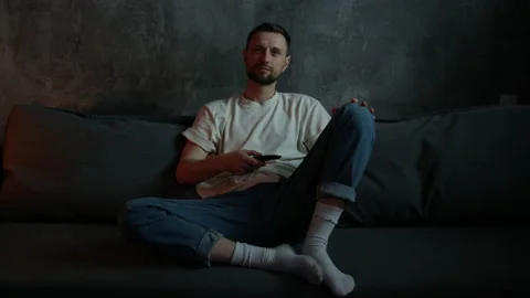 A man is sitting on the sofa and switching channels on the TV Stock Footage 197776658