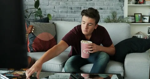 Man sitting on a sofa and using a phone watch tv eat popcorn feels an interest Stock Footage 82193426