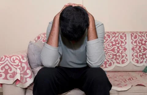 Man sitting on the sofa with his hands on his head and feeling sad Stock Photos