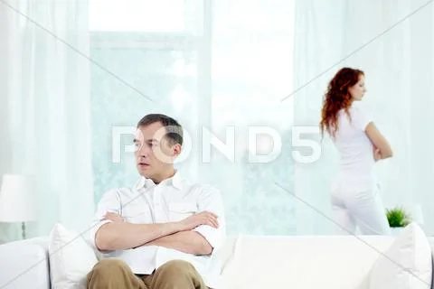 Man sitting on sofa with his wife standing on the background Stock Photos