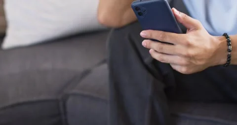 Man sitting on sofa holding blue phone, scrolling and picking popcorn while Stock Footage 339321344