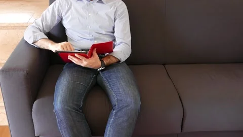 Man sitting on sofa at home uses his tablet, relaxing, side copy space Stock Footage 141377563