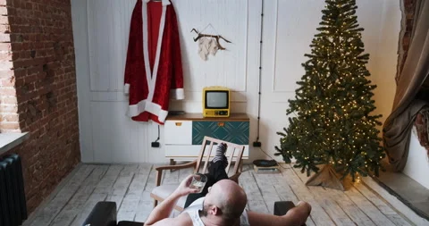 Man sitting on sofa at home waiting for Christmas, preparing to work as Santa Stock Footage 166018900