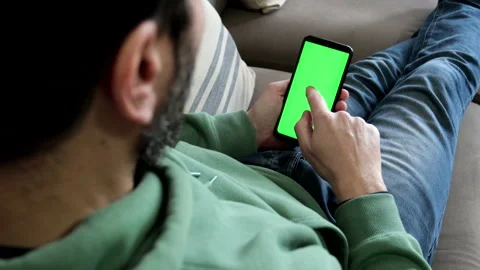 Man sitting on sofa makes single finger tap on smartphone green screen. Stock Footage 233914956