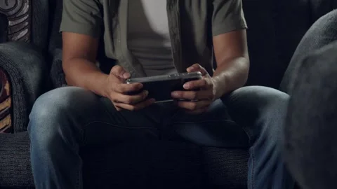 Man sitting on sofa playing mobile game repeatedly Stock Footage 317056057
