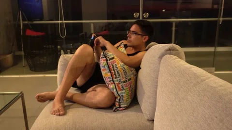 A man sitting on the sofa playing on the tv resting after work with cushions and Stock Footage 172269498