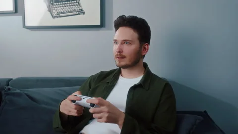 Man sitting on sofa playing video game with controller Vídeos de archivo 319544754