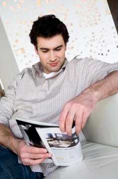 Man sitting on a sofa, reading a magazine Stock Photos