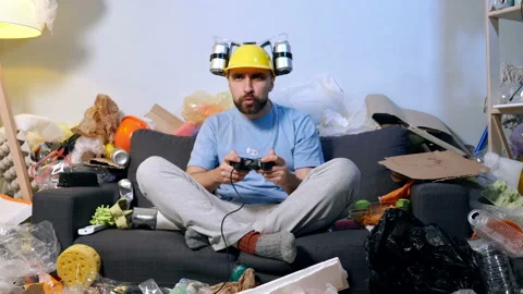 Man sitting on sofa in the room with garbage and playing video games. Stock Footage 120179517
