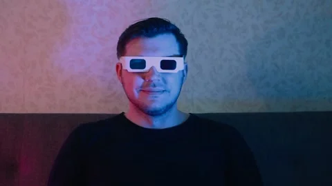 A man sitting on a sofa in stereo glasses watches TV and laughs a lot while Stock Footage 131368770