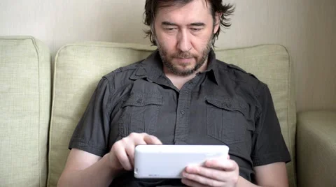 Man sitting on sofa with tablet computer in his living room Stock Footage 61150563