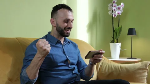 Man sitting on the sofa typing on smartphone and making fist in victory. Stock Footage 170953802