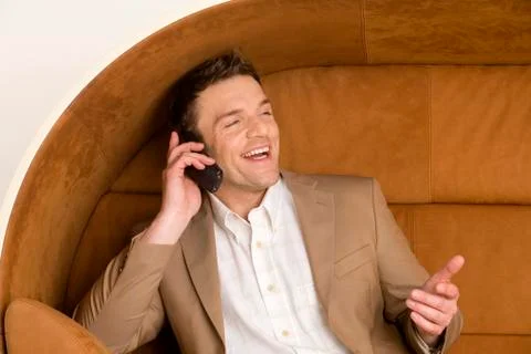 Man sitting on sofa using mobile phone, laughing Stock Photos