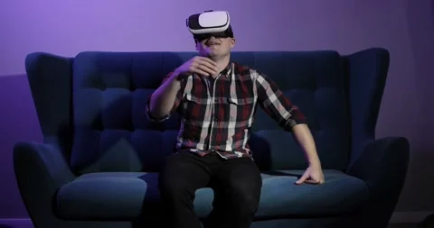 Man is sitting on sofa in virtual reality glasses and touching hands in air. Stock Footage 146680175