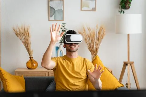 Man sitting on sofa wearing virtual reality goggles. Stock Photos